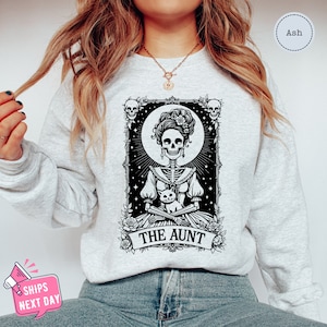 May include: A gray sweatshirt with a black and white graphic of a skeleton woman holding a cat. The graphic is in the style of a tarot card and says "The Aunt" at the bottom.