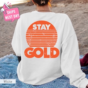 May include: White sweatshirt with an orange graphic of a sun with the text "STAY GOLD" on it.