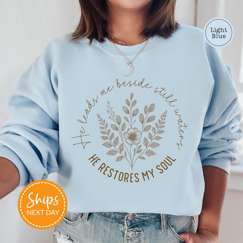 A woman wearing a light blue sweatshirt with a floral design and text printed on it.