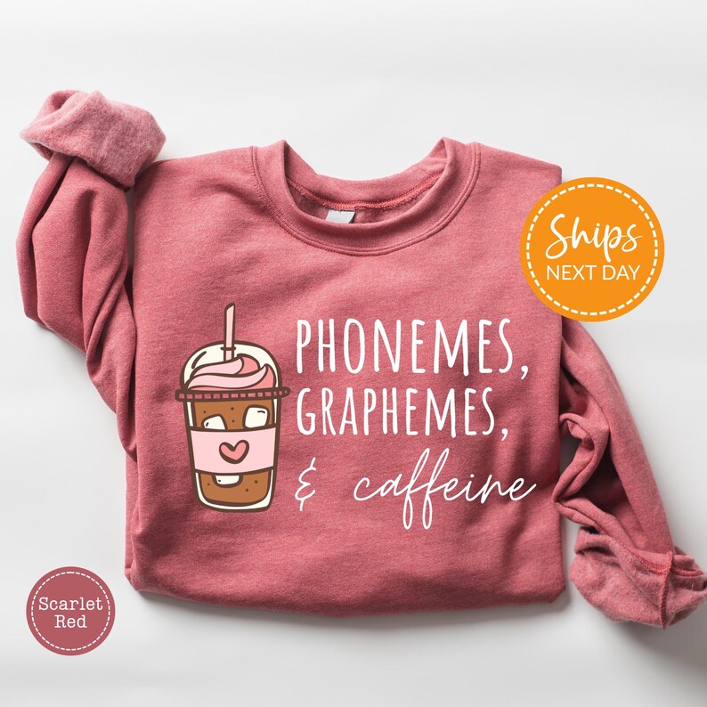 A pink sweatshirt with a graphic design of a coffee cup and text that reads "Phoneemes, Graphhemes, & caffeine".