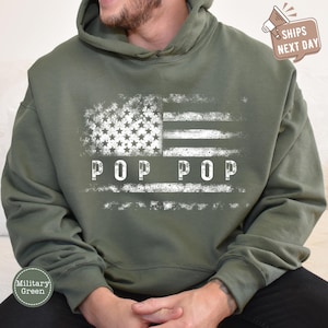 May include: A green hooded sweatshirt with a distressed white American flag design and the words "Pop Pop" printed below the flag.