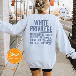 A person wearing a white sweatshirt with text printed on the back is walking on a sidewalk.