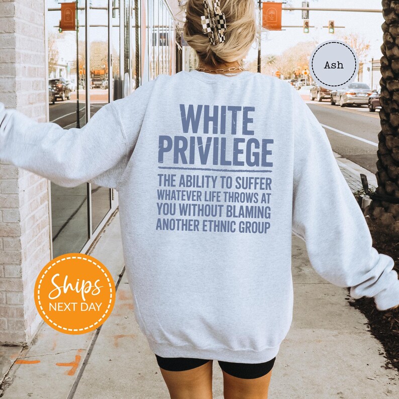 A person wearing a white sweatshirt with text printed on the back is walking on a sidewalk.