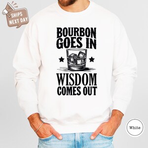 a man wearing a sweatshirt that says bourbon goes in wisdom comes out