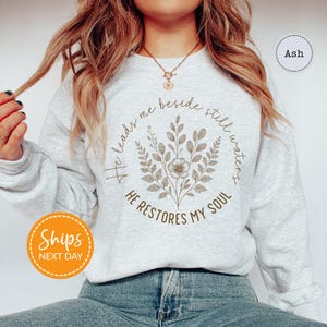 A woman wearing a gray sweatshirt with a floral design and text printed on it.