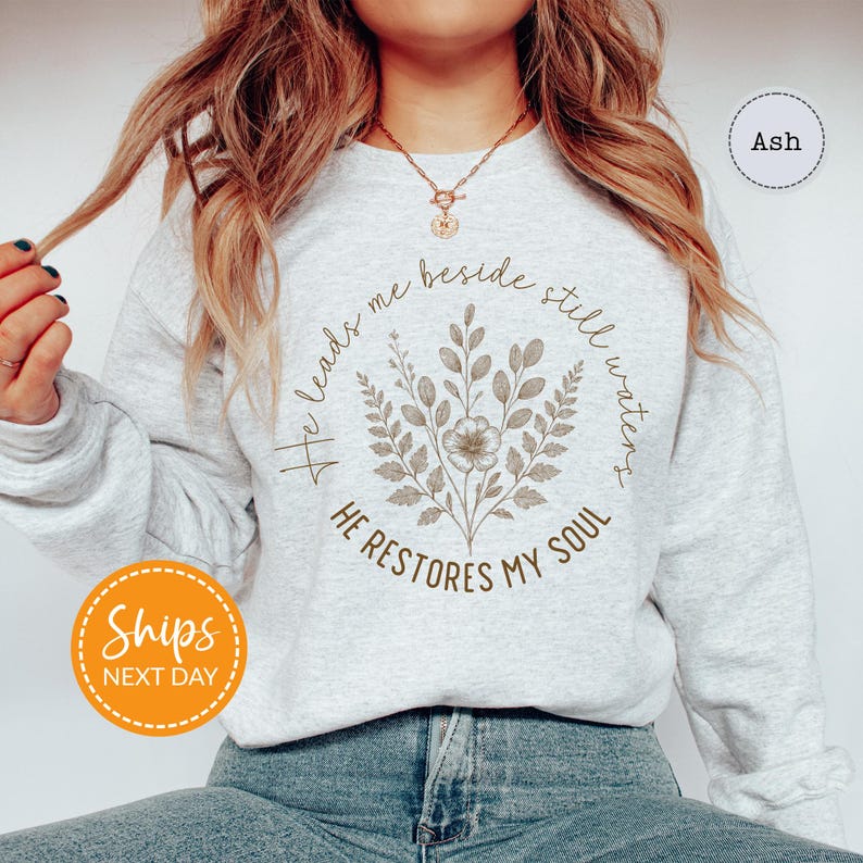 A woman wearing a gray sweatshirt with a floral design and text printed on it.