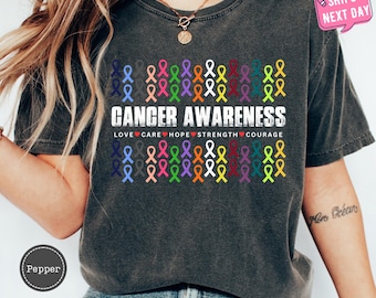 May include: A dark gray t-shirt with a faded look features a design of colorful ribbons with the text "Cancer Awareness" and the words "Love, Care, Hope, Strength, Courage" printed below.