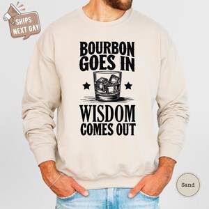 a man wearing a sweatshirt that says bourbon goes in wisdom comes out