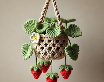 May include: A handmade crochet hanging planter featuring a beige basket with a woven design. The planter is adorned with green leaves, a white flower, and dangling red strawberries with green tops. The planter is suspended by a twisted rope.
