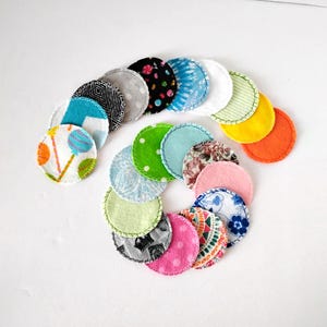 May include: A collection of colorful, circular reusable facial rounds. The rounds feature various patterns and colors, including floral, polka dots, and geometric designs. Each round is approximately 3 inches in diameter and has a stitched edge.