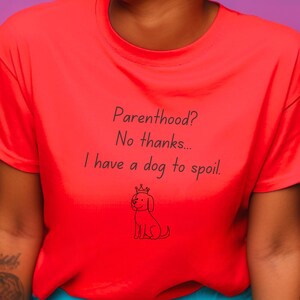 May include: A vibrant red t-shirt featuring the phrase "Parenthood? No thanks... I have a dog to spoil." A small drawing of a crowned dog is beneath the text. The shirt is made of a soft fabric.