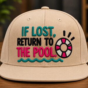 Può includere: Un cappellino da baseball beige con testo ricamato che recita IF LOST, RETURN TO THE POOL. Il design include una grafica a onda color ottanio, scritte nere e un'icona di salvagente rosa e bianco con accenti neri sul pannello frontale.