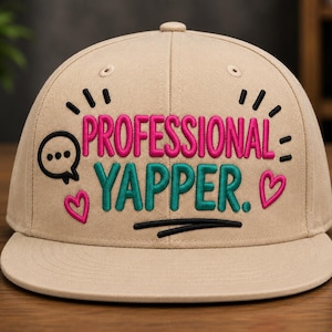 May include: A beige baseball cap featuring embroidered text that reads PROFESSIONAL YAPPER. The design includes a black speech bubble icon, two pink hearts, and black decorative lines, all stitched onto the front of the structured crown.