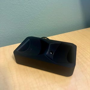May include: A black charging case for wireless earbuds. The case has a smooth, matte finish and two circular indents for the earbuds.