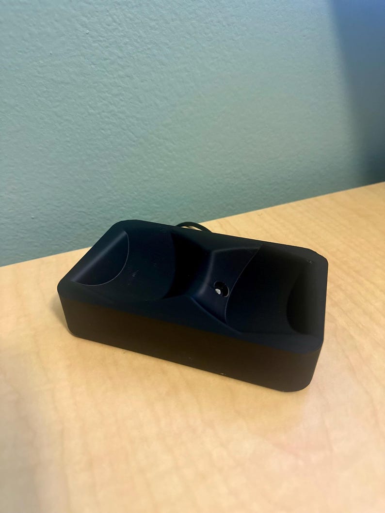 May include: A black charging case for wireless earbuds. The case has a smooth, matte finish and two circular indents for the earbuds.