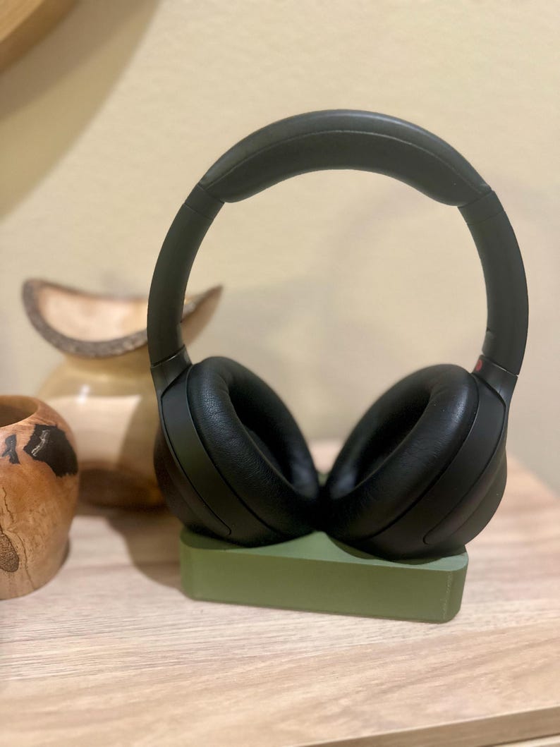 May include: Black over-ear headphones with a padded headband resting on a green stand.