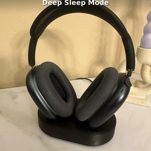 May include: Black over-ear headphones with gray ear cushions are displayed on a black charging stand. The text "Wireless Charging" and "Deep Sleep Mode" are visible at the top of the image.