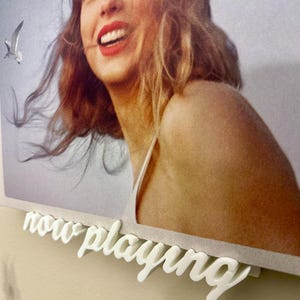Könnte beinhalten: Ein weiß gerahmtes Foto einer Frau mit blonden Haaren, die lächelt. Das Foto hängt an einer Wand mit einem weißen Schild, auf dem "now playing" steht.