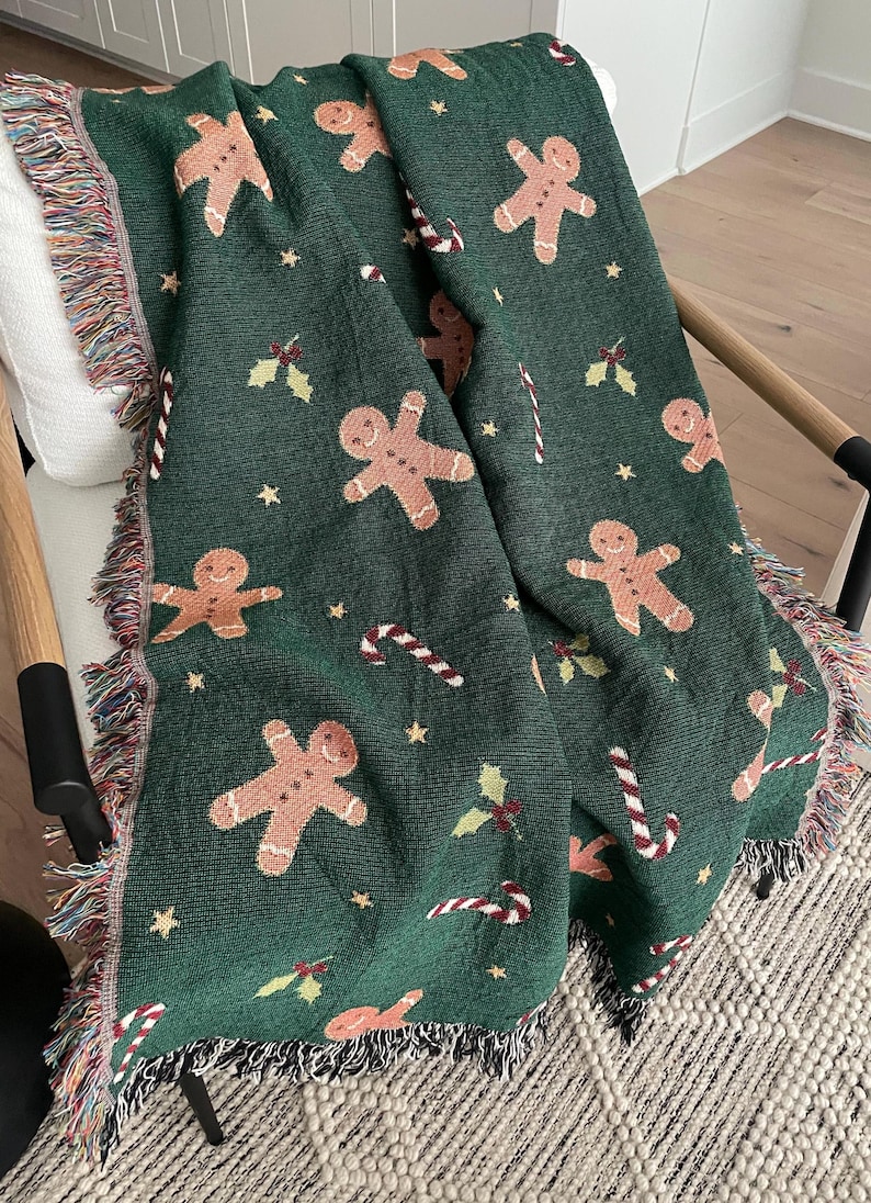 Cozy green woven Christmas throw blanket with gingerbread men, candy canes, and holly draped over a chair — festive holiday décor and winter gift idea.