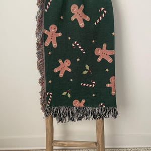 Cozy green woven Christmas throw blanket featuring gingerbread men, candy canes, holly leaves, and gold stars — festive holiday home décor gift.