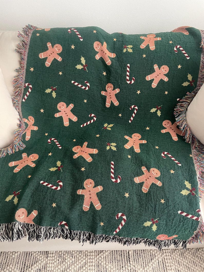 Green woven Christmas throw blanket with gingerbread men, candy canes, holly, and stars displayed on a sofa — cozy festive home décor and holiday gift.