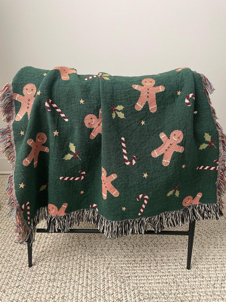 Green woven Christmas throw blanket with gingerbread men, candy canes, holly, and stars draped over a chair — festive holiday décor and cozy winter gift.