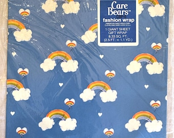 May include: Blue Care Bears fashion wrap with a repeating pattern of rainbows, clouds, and hearts. The gift wrap is in a plastic sleeve and features the Care Bears logo and product information.