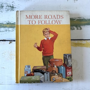 以下が含まれることがあります： 赤い文字で「More Roads To Follow」と書かれた黄色の本。表紙には、困惑した表情の若い男の子が、スーツケースや荷物に囲まれている様子が描かれている。