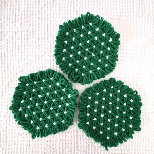 Puede incluir: Tres posavasos de ganchillo verde y blanco con un patrón geométrico. Los posavasos son redondos y tienen un centro blanco con bordes verdes.