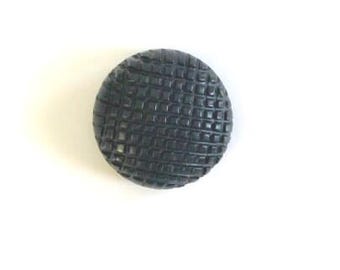 May include: A circular black button featuring a raised grid pattern across its entire surface. The button has a slightly domed shape with a textured, checkered design consisting of small, uniform squares arranged in a repeating grid formation.