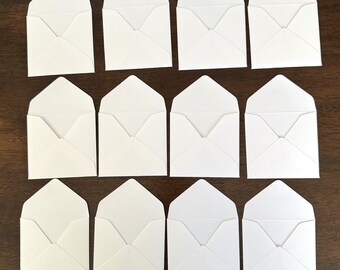 May include: Twelve white envelopes with a pointed flap. The envelopes are arranged in three rows of four.