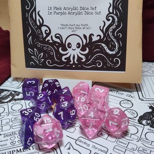 Op de afbeelding: Een set roze en paarse acryl dobbelstenen. De dobbelstenen worden gepresenteerd op een wit oppervlak met karakterbladen. De verpakking leest "1X Pink Acrylic Dice Set" en "1x Purple Acrylic Dice Set". De verpakking heeft ook een octopus illustratie.