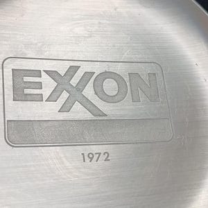 Może przedstawiać: Srebrny metalowy talerz z wygrawerowanym napisem "EXON" i rokiem "1972".