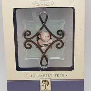 Puede incluir: Portafotos Hallmark Keepsake Ornament en una caja. El adorno tiene un marco de metal decorativo con una pequeña foto de un bebé. La caja dice "The Family Tree" y "Joy, Smiles, Fun".