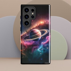 May include: A black phone case with a galaxy and planet design. The case features a dark blue background with a swirling nebula, a bright orange star, and a ringed planet in the center.