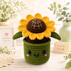 Peut inclure: Un tournesol crocheté à la main dans un pot vert avec un visage souriant. La fleur a des pétales jaunes, un centre marron et des feuilles vertes. Le pot a des yeux noirs et des joues roses. Une petite carte dit "merci".