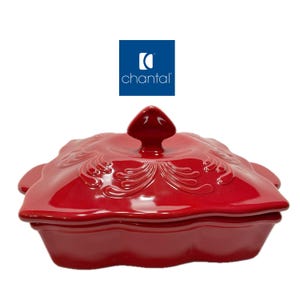 May include: A glossy red ceramic square baking dish with a matching lid featuring a central handle and embossed scrollwork patterns. The lid is topped with a pointed knob. The brand name Chantal is displayed in a blue square logo above the dish.