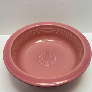 Puede incluir: Un cuenco de cerámica de color rosa empolvado con forma redonda, que presenta un borde ancho y plano y una serie de surcos circulares concéntricos grabados a lo largo de la pared interior y en el centro de la base, creando un diseño uniforme.