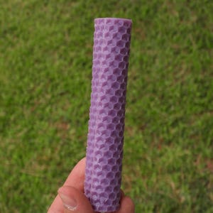 Puede incluir: Una vela de color morado con forma de panal. La vela está hecha de cera de abejas y tiene un patrón hexagonal.