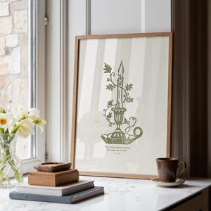 May include: A framed print with a green candle illustration in a decorative holder with floral details. The print has a light background with vertical stripes and a wooden frame. The quote "The word is a lamp unto my feet, And a light unto my path." is at the bottom.