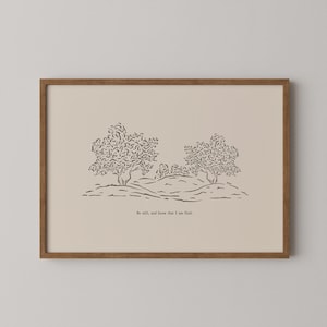 May include: A framed art print featuring a minimalist landscape illustration. The artwork depicts two trees and rolling hills in black ink on a beige background. The text "Be still, and know that I am God" is printed at the bottom.