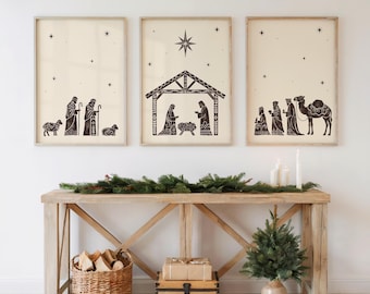 May include: Three framed art prints with a cream background and black illustrations depicting a nativity scene. The prints show shepherds, the holy family, and the three wise men. The prints are displayed above a wooden console table.