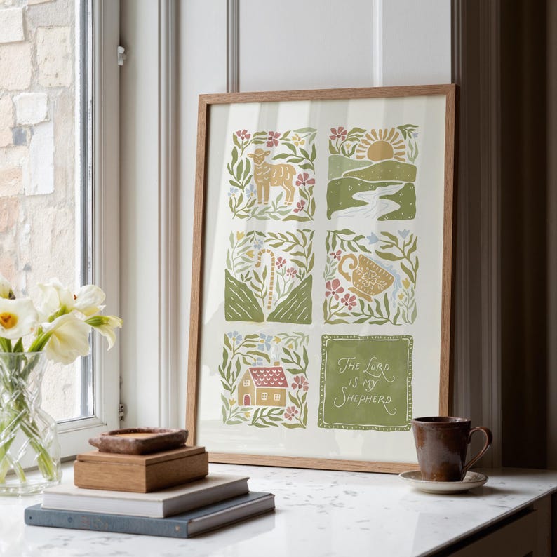 May include: A framed art print with a light wood frame. The print features six illustrated squares with a lamb, landscape, and house. The bottom right square has the text "The Lord is my Shepherd" in green.