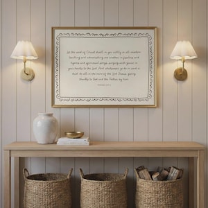 Peut inclure: Une impression encadrée avec une bordure dorée affiche le texte "Que la parole du Christ habite en vous..." sur un fond crème. L'impression est suspendue au-dessus d'une console en bois avec des paniers tressés et un vase blanc.