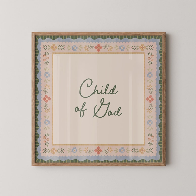 May include: A framed print featuring the text "Child of God" in a cursive font. The print has a beige background with a floral border in blue, pink, and yellow. The frame is a light brown colour.