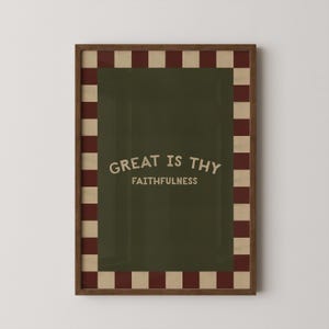 May include: A framed art print with the words "GREAT IS THY FAITHFULNESS" in a vintage font. The artwork features a dark green background with a red and beige checkered border and a brown frame.