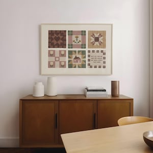 Puede incluir: Obra de arte enmarcada con seis diseños de bloques de edredón en tonos marrones, verdes y rosas. La obra de arte incluye el texto "BUT AS FOR ME AND MY HOUSE WE WILL SERVE THE LORD". La obra de arte se exhibe sobre un mueble de madera.
