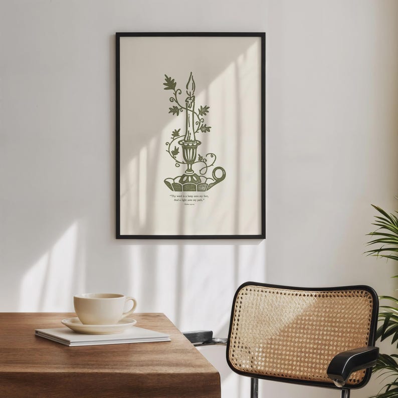 May include: A framed print with a green illustration of a candle in a decorative holder, decorated with leaves. The artwork is set against a cream background, with text at the bottom. The frame is black.