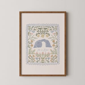 May include: A framed art print with a floral border and the words "He is Risen." The image shows a blue tomb with a stone removed, surrounded by pastel-colored flowers. The frame is a warm brown.