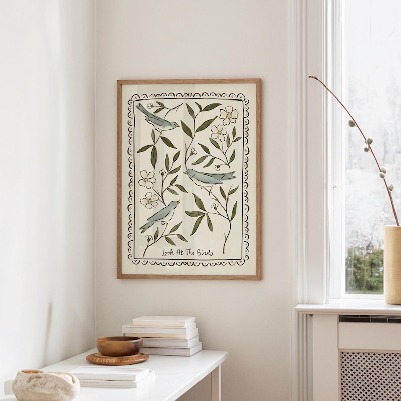 Pu&ograve; includere: Stampa artistica incorniciata con tre uccelli blu appollaiati tra foglie verdi e fiori bianchi. L'opera d'arte &egrave; ambientata su uno sfondo color crema e incorniciata in una cornice di legno marrone chiaro. Il testo "Look At The Birds" &egrave; in basso.